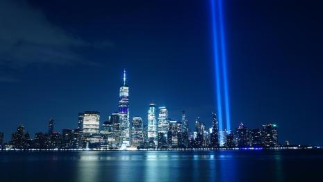 9/11 memorial of nighttime NYC skyline with two spotlights in place of the towers.