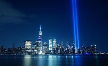 9/11 memorial of nighttime NYC skyline with two spotlights in place of the towers.